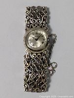 Full view of silver filigree bracelet watch with round dial and Roman numerals