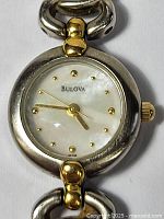 Close-up of the watch face showing the Bulova brand, mother of pearl dial with gold dot hour markers and gold-tone case accents.