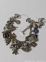Photo of the full charm bracelet laid out to show all charms including heart lock clasp and various detailed charms