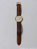 Full view of men's wristwatch with dark brown leather strap and gold-tone round case on a white background.