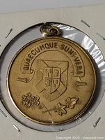 Close-up image of front of gold toned medal pendant with detailed coat of arms and floral designs.