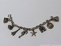 Full view of the charm bracelet laid flat showing the chain and all 7 attached charms including Eiffel Tower, seahorse, starfish, coin, and building designs.