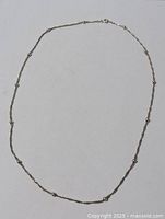 Full view of the sterling silver twisted ball chain necklace laid flat on a white surface.