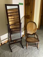 The full-length dressing mirror with dark wooden frame stands next to the antique rocking chair on carpeted floor.