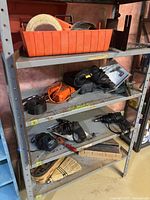 Metal shelving unit with various power tools and hand tools arranged on four shelves including drills, sanding discs, and cords.
