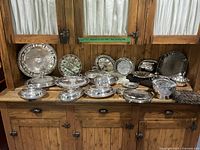 Wide view of all silver-plated pieces displayed on wood cabinet
