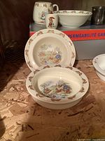 Photo showing 3 ceramic baby dishes with Bunnykins design: a bowl, a plate, and a mug, all decorated with rabbit motifs and pastel colors.