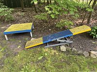 Outdoor shot of blue and yellow seesaw and raised platform in wooded backyard
