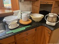 Overview of kitchen counter showing mixing bowls, Lazy Susan, ceramic jar, gravy boat, food processor and Corning Ware casseroles.