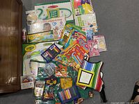 Photo of assorted kids craft supplies including paper, activity books, paints, and crayons spread on the floor.