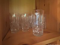 Twelve clear crystal water glasses arranged on wooden shelf with some glasses grouped in front, showing their consistent cut glass pattern.