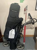Full view of collapsible golf bag on golf cart with red and white flag pole and golf practice net behind.