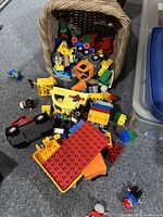 Photo of Lego blocks and mini figures with some Duplo pieces mixed in, showing a variety of colors and some loose components on a carpeted floor.