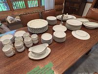 Full overview of the Elite Limoges China set arranged on a wooden dining table with a mix of plates, bowls, cups, a gravy boat, and candle holders.
