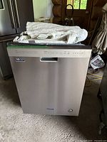 Full frontal view of stainless steel Maytag dishwasher with taped top and packaging materials