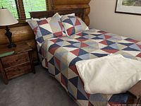 Full view of bed with quilt, pillows and sheet on solid wood mission style frame, nightstand and lamp visible