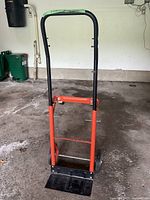 Orange and black moving dolly with adjustable handle from front view.