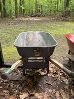 Front view of the wheelbarrow showing gray metal tub and wooden handles with grips.