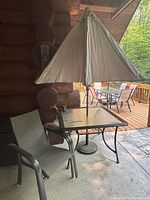 Patio table with umbrella inserted through center, two patio chairs beside the table, all on a concrete floor with a log cabin wall in the background