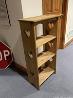 Angled view showing natural pine wood with three shelves and heart cutouts on the sides.