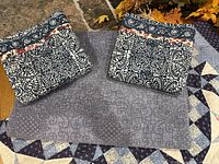 Two embroidered pillow shams with floral and geometric patterns on a navy background, folded on top of an embroidered comforter with matching design and a solid gray cloth underneath.