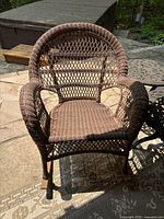 Photo of brown woven resin patio chair with curved arms and diamond weave back, showing full front view.