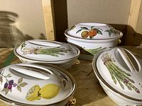 Overview of four covered dishes showing asparagus, lemon/blackberry, and orange motifs with lids on.