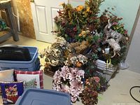 Wide view showing assortment of artificial seasonal floral and foliage decor clustered around blue totes and decorative pillows.