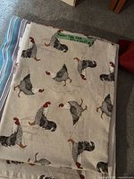 Five folded tablecloths in a stack, showing various patterns and colors.