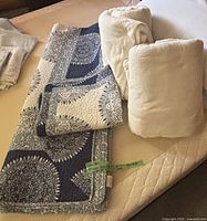 Photo showing folded twin comforter and pillow sham with blue and white mandala patterns, alongside two folded off-white soft fleece blankets on a bed