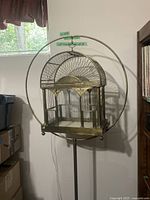 Full view of the vintage brass birdcage on stand with circular frame.