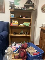 Shelves with various vintage children's toys including animal figurines, fabric teddy bear, toy cash register, displayed beside a blue sofa.