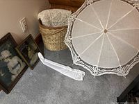 Overview of lot with two framed prints leaning against wall, basket with throw inside, and parasol open on floor with sleeve