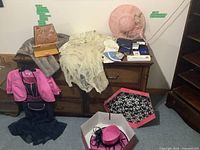 Full lot display with dress, mink stole, hats, purse, jackets, and wallets shown on and near a wooden dresser.