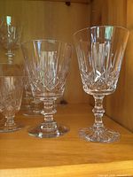 Photo showing 2 Waterford stemmed glasses with detailed cut crystal patterns on wooden shelf.