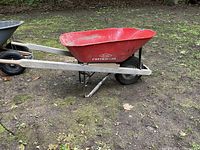 Side view of red True Temper contractor wheelbarrow with inflated tire on muddy ground.