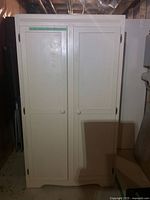 Front view of closed white wooden cabinet with two doors and round knobs in a basement setting.