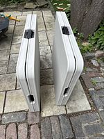 Two Elite Home folding tables in folded position showing black handles and folded legs, positioned on stone patio outdoors.