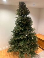 Full height photo of assembled 7ft green artificial Christmas tree with visible metal base, standing in a room corner.