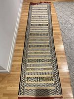 Full length view of the rectangular cotton rug laid on wooden floor, showing its geometric pattern and fringed ends.