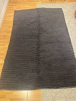 Full view of the rectangular gray chunky knit wool rug laid on wooden floor, showing the solid knit pattern and size.