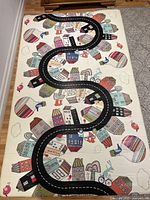 Play mat showing colorful cityscape with buildings, hot air balloons, birds and a road winding through it.