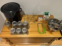 Photo showing full set including black enamel canning pot with lid and handles, metal rack insert, 8 glass jars with metal lids, stainless steel food mill, jar lifter and lid lifter with green grips, plus Bernardin lids in packaging.