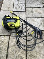 Overview showing pressure washer unit, spray gun wand, and coiled high pressure hose laid on stone patio