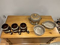 Set of 6 brown and beige ceramic French onion soup bowls with handles and ridged exterior on wooden chest, three additional vintage Canadian ceramic serving pieces including a lidded pot, round bowl, and oval dish.