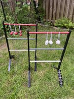 Two black and red ladder stands on grass with six bolas hanging