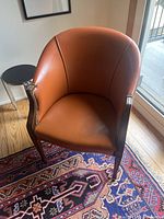 Front diagonal view of orange faux leather chair showing nailhead trim and wooden legs.