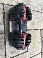 Adjustable dumbbell resting on its black plastic stand on a stone surface, showing weight selector and handle details