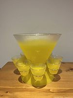 Front view of the yellow glass punch bowl and six matching cups arranged around its base, showing the ribbed texture and gradient color.