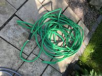 Green coiled garden hose with black connectors laid on stone ground.